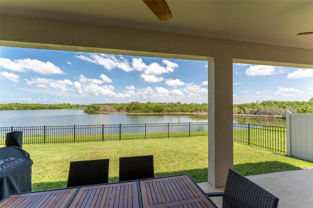 A covered patio overlooks a grassy lawn, a black metal fence, and a lake — 3719 LIVELY CORAL PLACE, BRADENTON, FL
