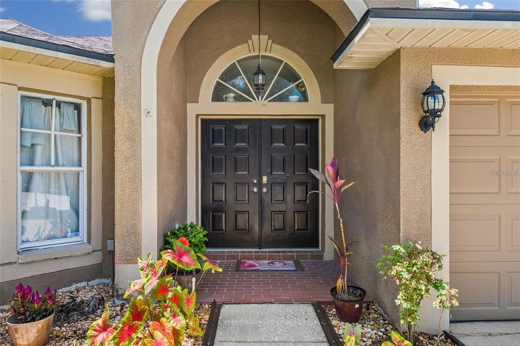 A front entryway features double black doors under an arched transom window and brick porch — 4007 HARBOR LAKE DRIVE, LUTZ, FL