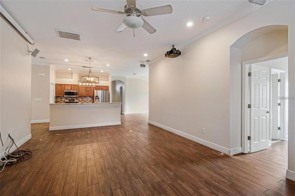 A living room with wood-look tile floors, a ceiling fan, and an open kitchen beyond — 4007 HARBOR LAKE DRIVE, LUTZ, FL