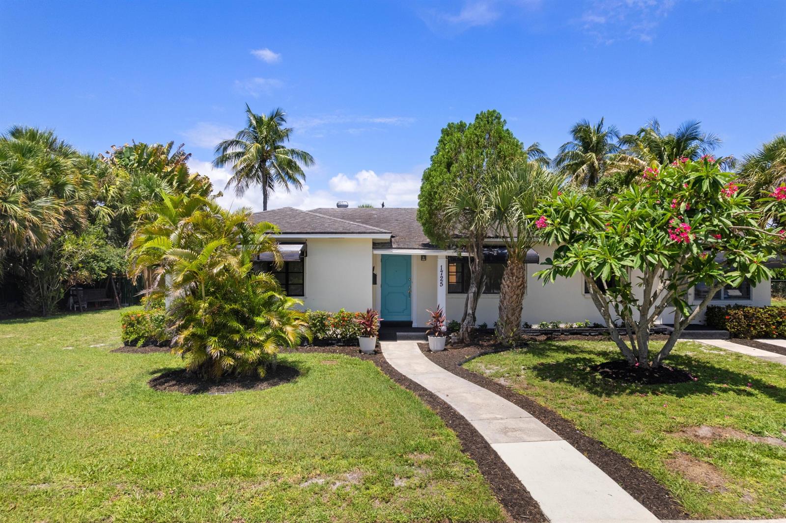 A single-story house with a light-colored exterior, a turquoise front door, and lush landscaping — 1725 N Lakeside Drive, FL 33460, FL