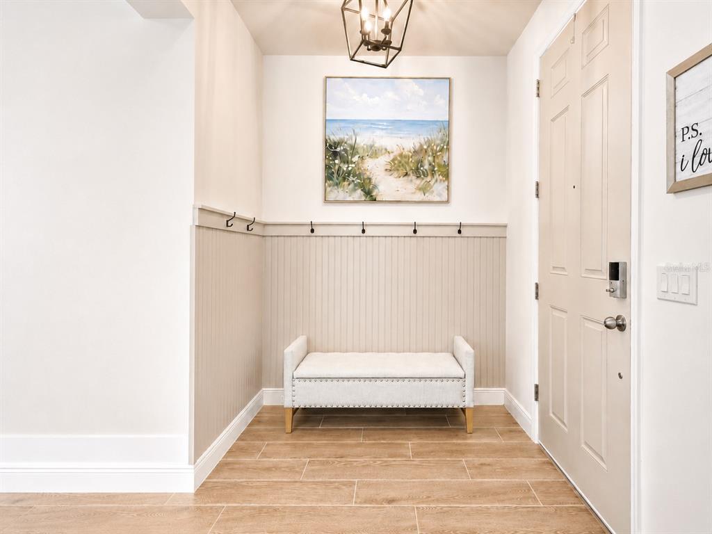An entryway features a beige bench, beadboard wainscoting with hooks, and a coastal wall painting — 5046 DOWN COURT, ST CLOUD, FL