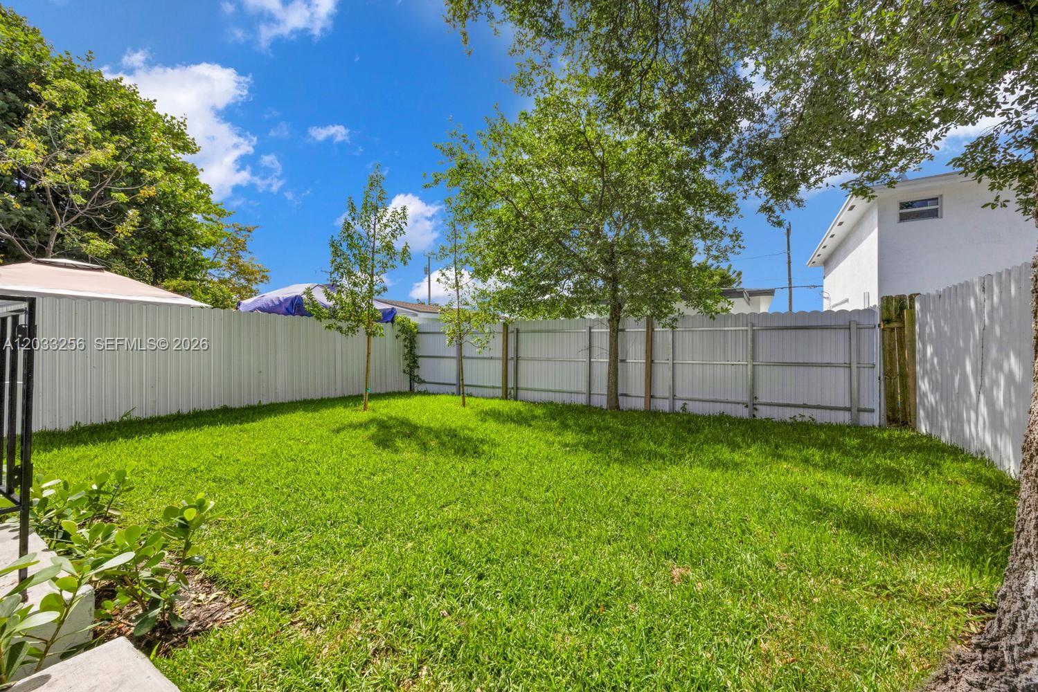 A grassy backyard features a white vinyl fence, several trees, and a patio umbrella — 2780 NW 44th St, Miami FL 33142, MIAMI, FL