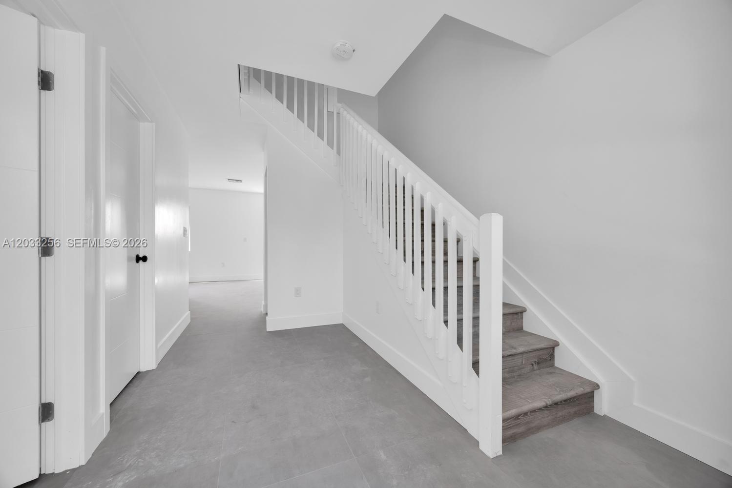 A staircase with wooden treads and white railings stands in a room with gray flooring — 2780 NW 44th St, Miami FL 33142, MIAMI, FL