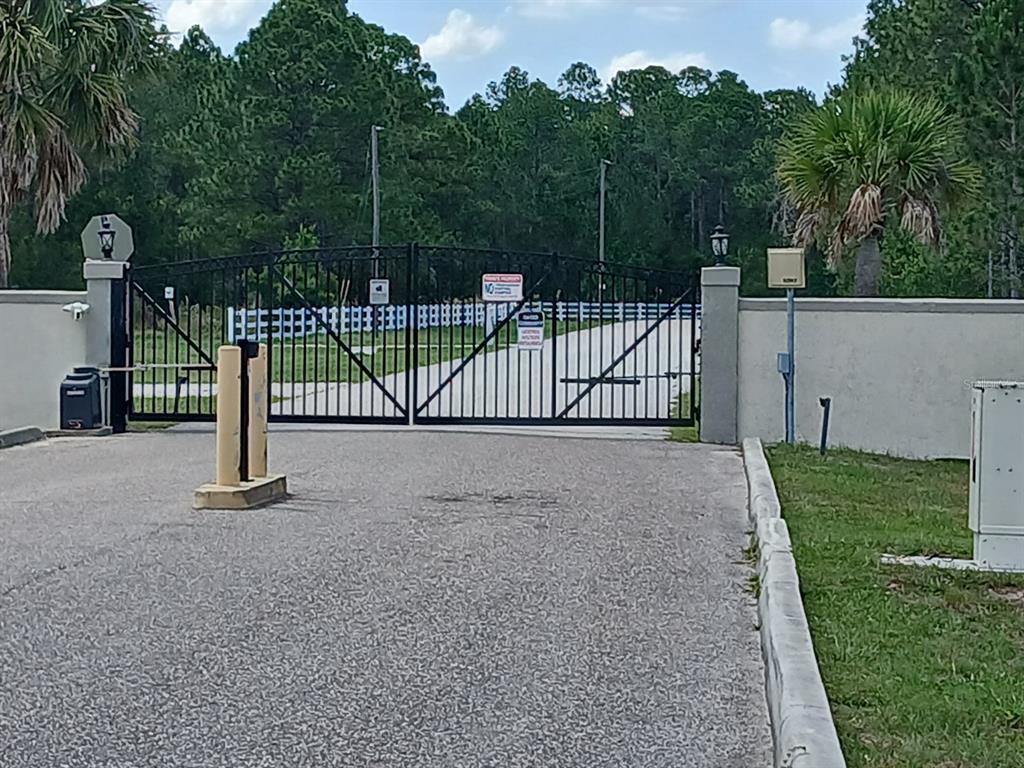 A black metal gate secures the entrance to a paved driveway surrounded by trees — 1102 HIDDEN PALMS DRIVE, DAVENPORT, FL