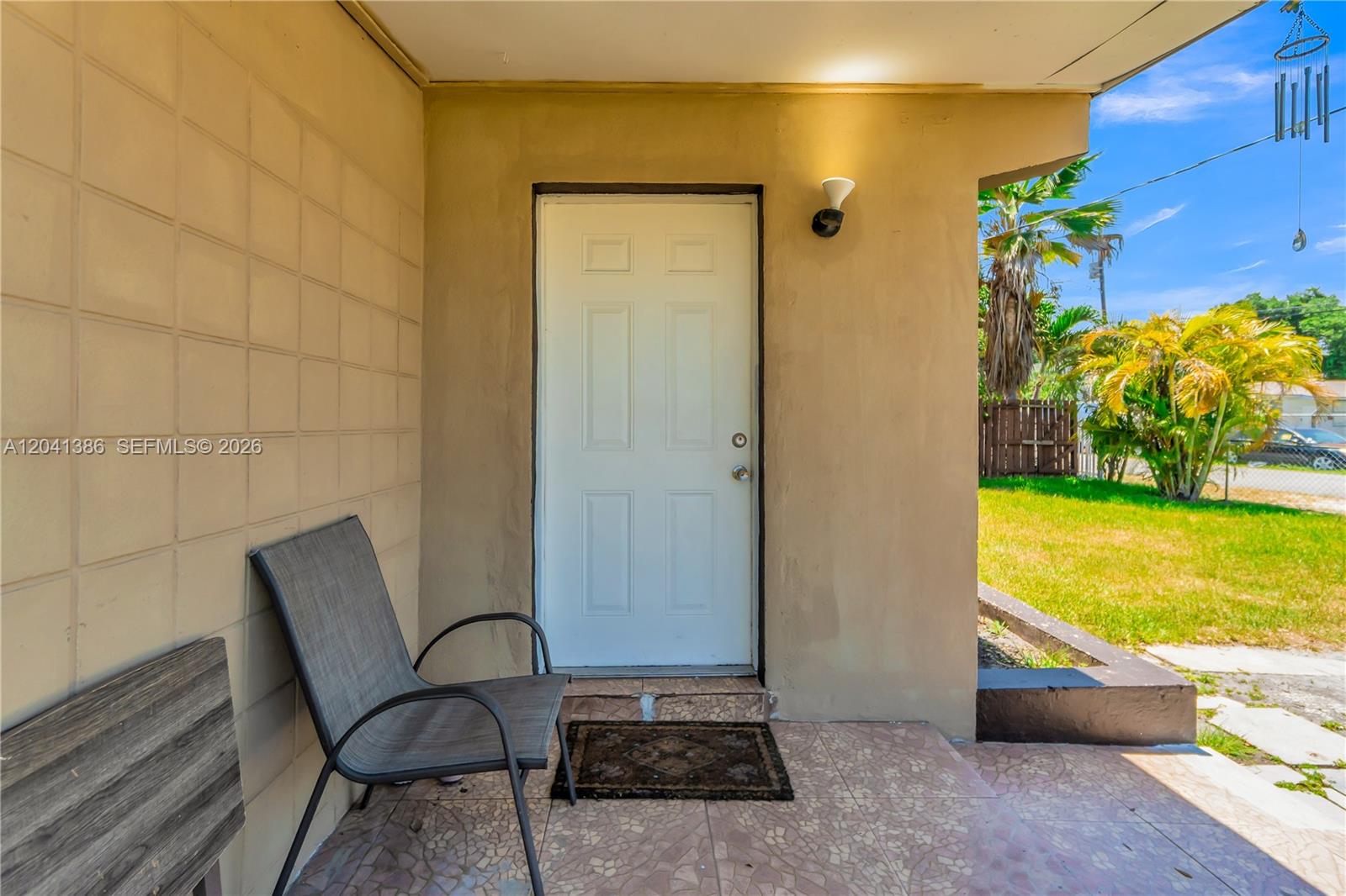 A white door opens onto a tiled porch with a chair and a wall light — 2910 NW 47th St, Miami FL 33142, MIAMI, FL