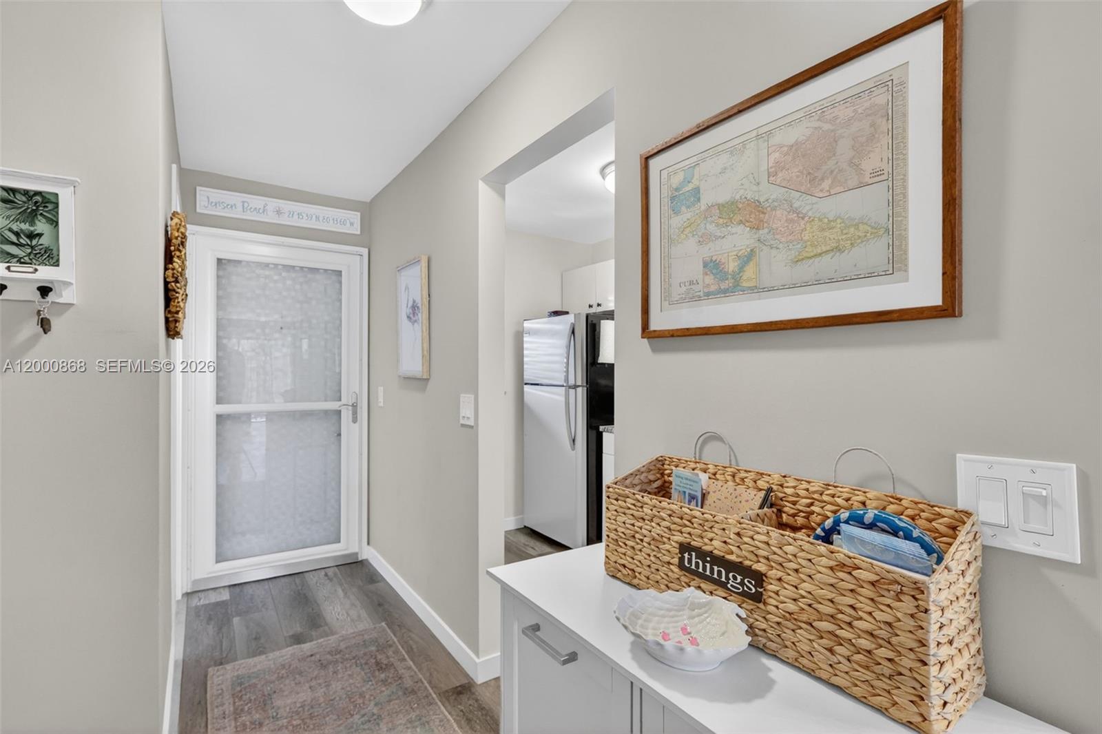 A hallway with a white door, a framed map, and a woven basket on a cabinet — 9425 S Ocean Dr # 67, Jensen Beach FL 34957, JENSEN BEACH, FL