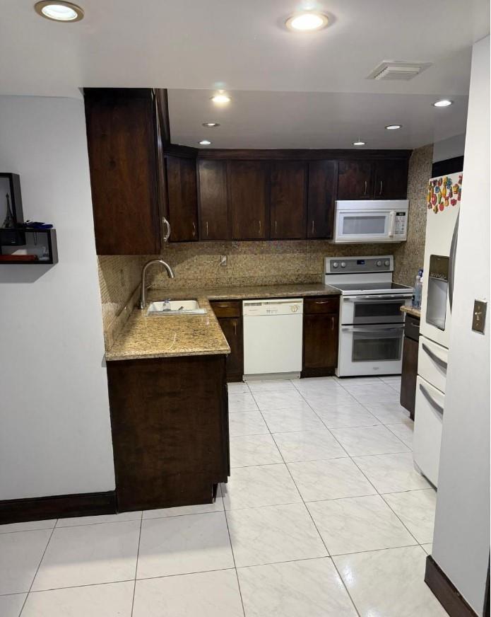 A kitchen features dark wood cabinets, granite countertops, a white dishwasher, and light tile flooring — 1833 S Ocean Drive # 1209, FL 33009, FL