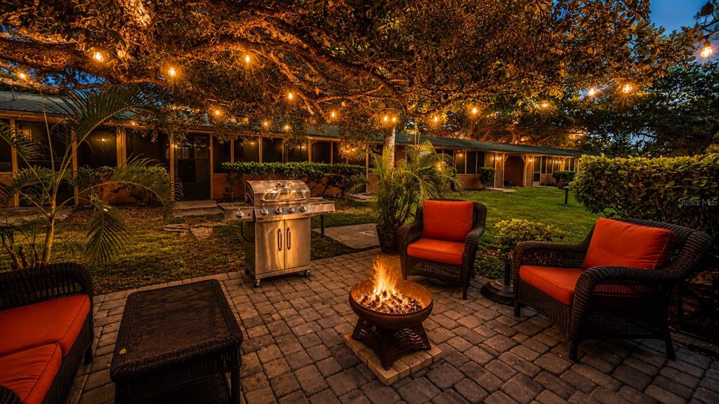 A patio with a fire pit, grill, and wicker furniture under string lights at dusk — 3200 RIVER RANCH BOULEVARD UNIT 303, LAKE WALES, FL