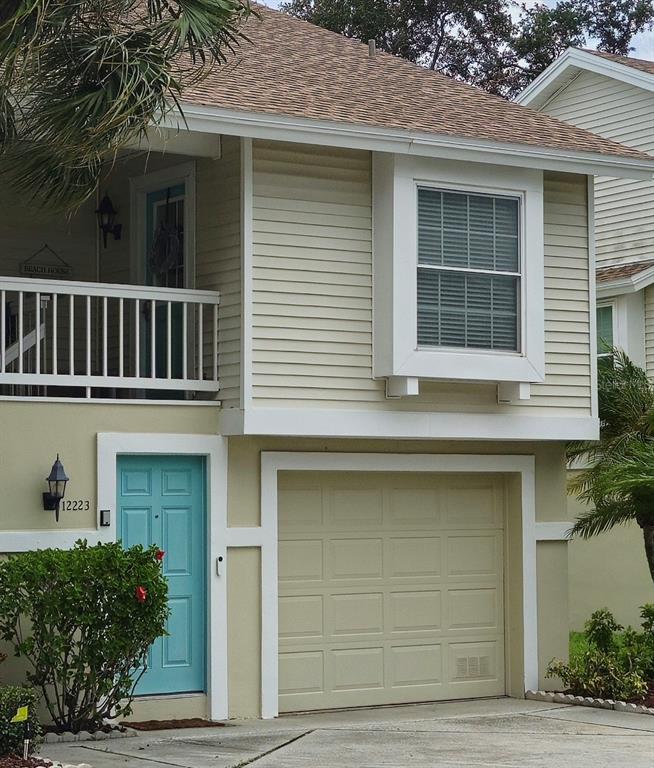 A two-story house exterior features a light blue front door, a garage, and a balcony — 12223 SUN VISTA COURT E, TREASURE ISLAND, FL