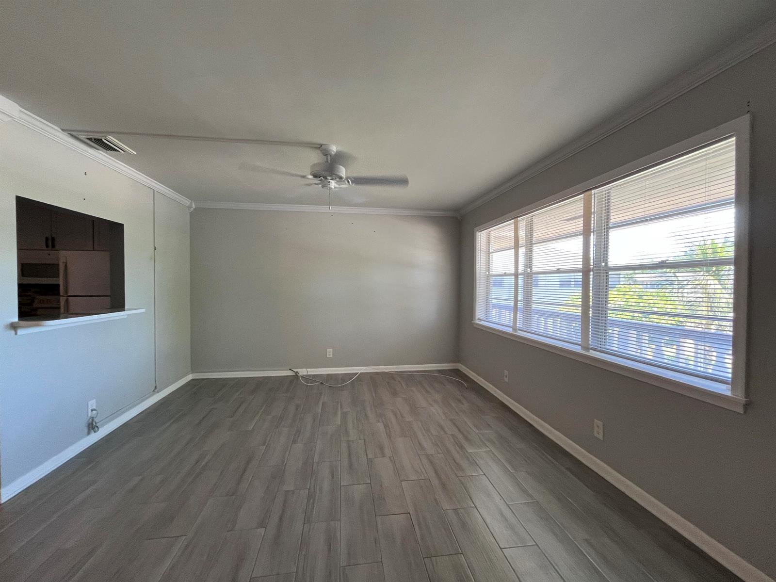 An empty living room with gray walls, wood-look tile flooring, a ceiling fan, and windows — 49 B Cambridge B, West Palm Beach FL 33417, WEST PALM BEACH, FL