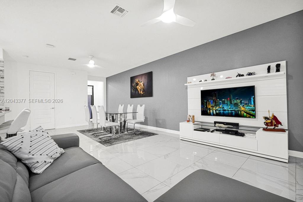 A modern living and dining room features white tile floors, a gray accent wall, and a television — 10533 NW 81st St, Doral FL 33178, DORAL, FL