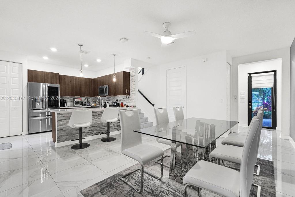 A modern kitchen and dining area features white tile floors, dark wood cabinets, and glass furniture — 10533 NW 81st St, Doral FL 33178, DORAL, FL