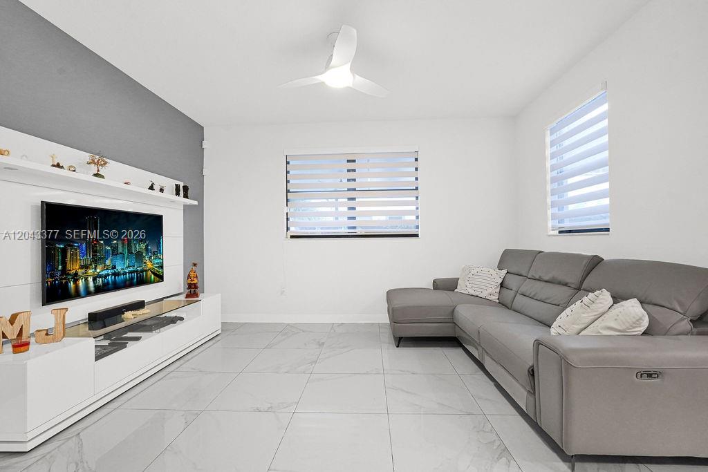A living room features a grey sectional sofa, a wall-mounted television, and tiled flooring — 10533 NW 81st St, Doral FL 33178, DORAL, FL
