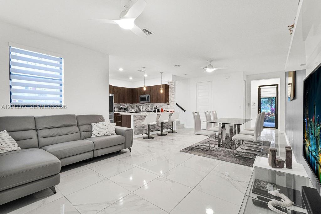 A modern open-concept living room and kitchen featuring white tile floors and a gray sofa — 10533 NW 81st St, Doral FL 33178, DORAL, FL