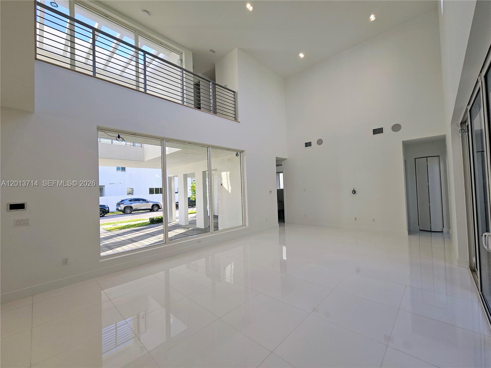 A spacious, minimalist living room features white tile floors, high ceilings, and a glass balcony — 10289 NW 75th Ter # 10289, Doral FL 33178, DORAL, FL