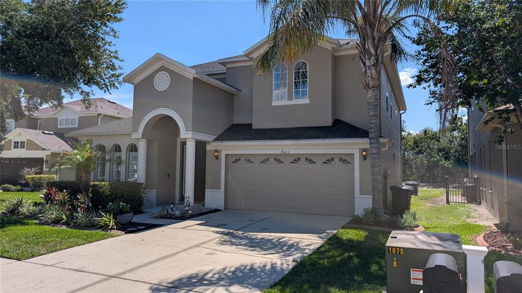 A two-story suburban house with a tan stucco exterior, a two-car garage, and a palm tree — 4023 HUNTINGDALE COURT, WESLEY CHAPEL, FL