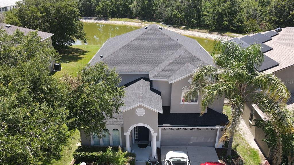An aerial view shows a two-story house with a gray roof, garage, and backyard pond — 4023 HUNTINGDALE COURT, WESLEY CHAPEL, FL