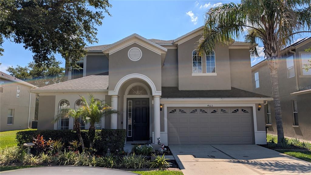 A two-story suburban house with a beige stucco exterior, arched entryway, and a two-car garage — 4023 HUNTINGDALE COURT, WESLEY CHAPEL, FL