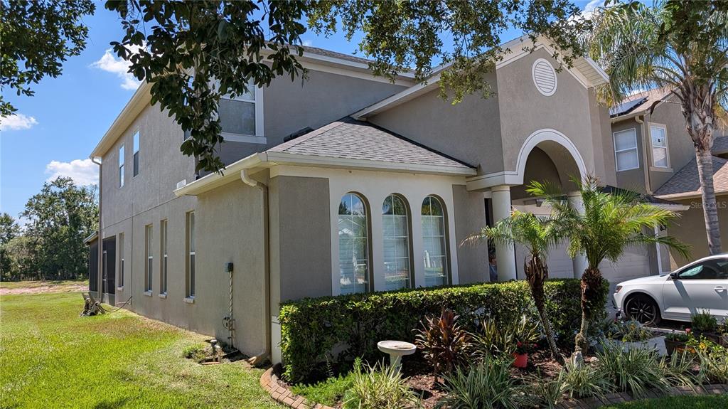 A two-story stucco house with arched windows, a front hedge, and a side lawn — 4023 HUNTINGDALE COURT, WESLEY CHAPEL, FL