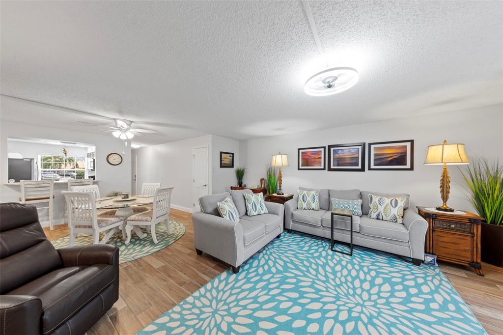 A living room and dining area feature light gray furniture, wood-look flooring, and blue patterned rugs — 7104 NANTUCKET CIRCLE UNIT 3, NORTH FORT MYERS, FL
