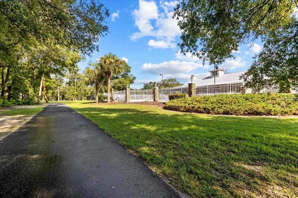 A paved path leads toward a fenced pool area surrounded by trees and green grass — KATHERINE WAY, FANNING SPRINGS, FL