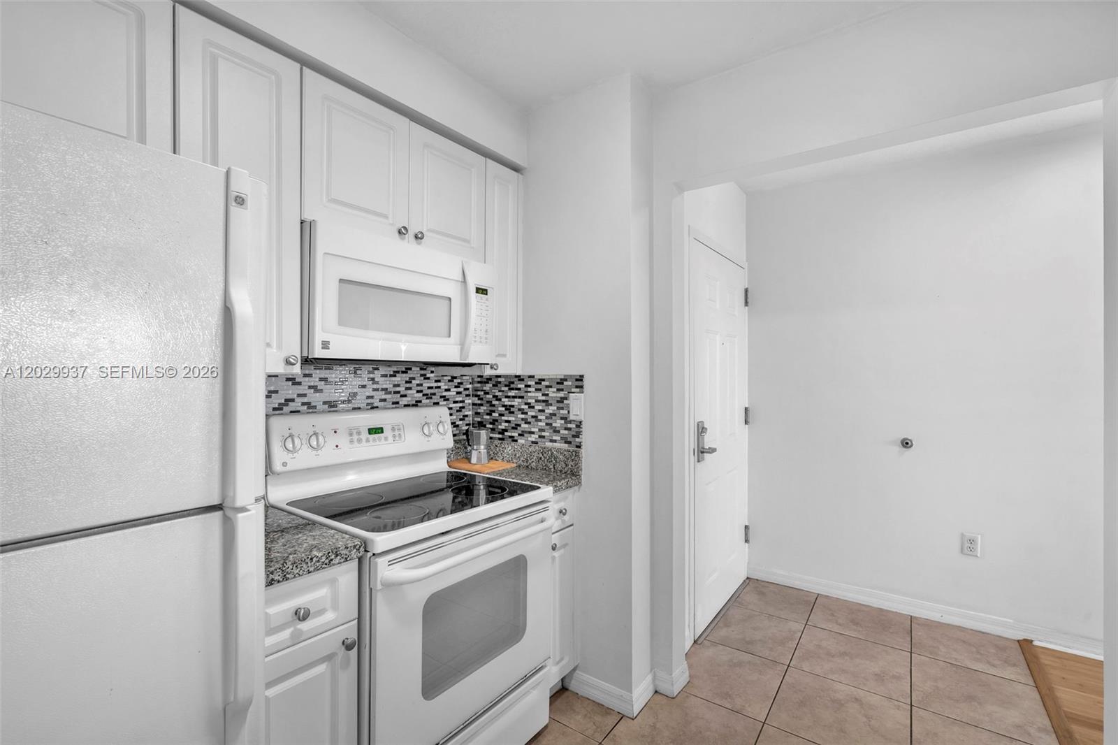 A kitchen features white cabinets, a white stove, a microwave, and a tiled backsplash — 900 SW 8th St # 1103, Miami FL 33130, MIAMI, FL