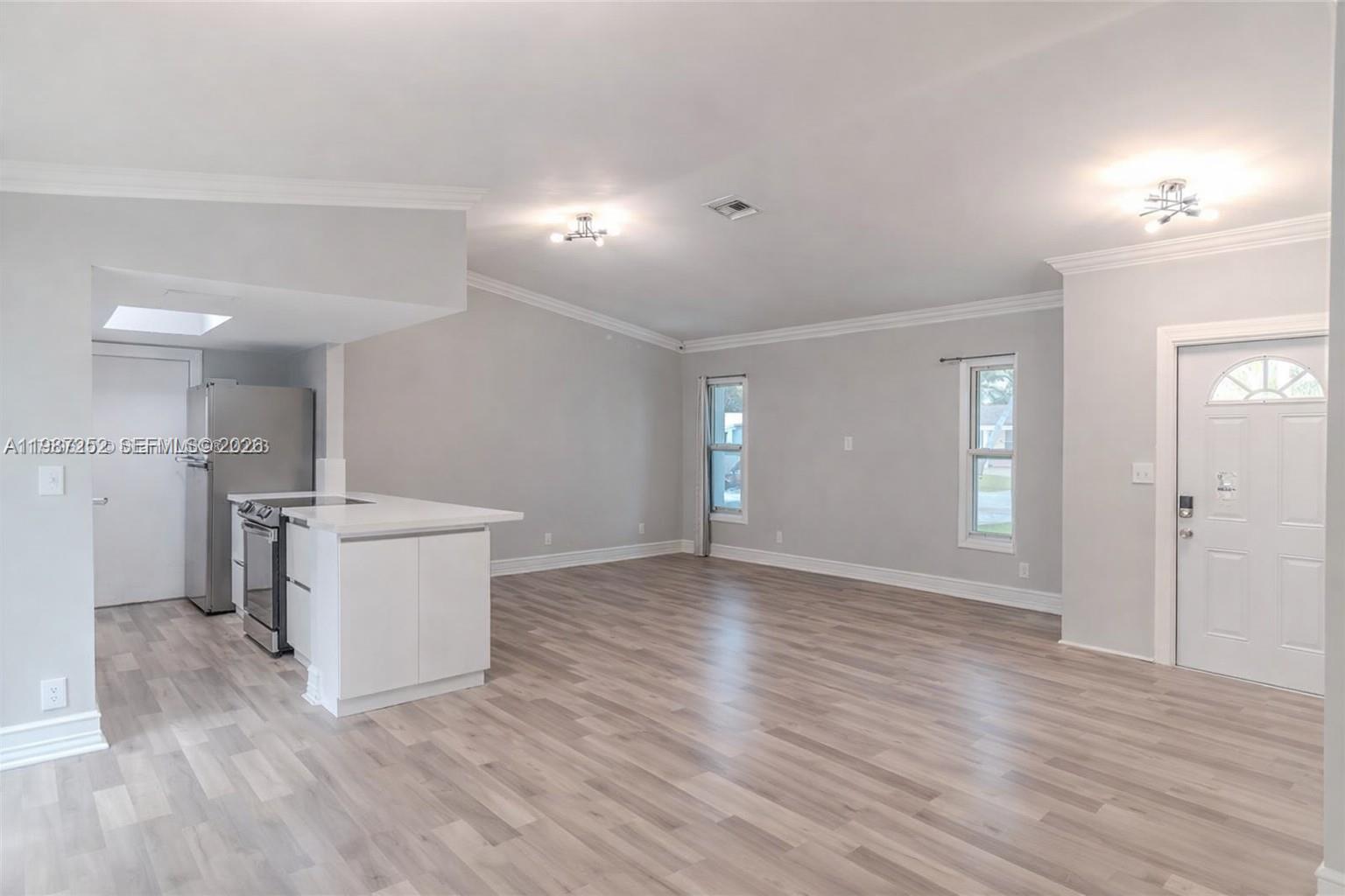 An open-concept living area features light wood-look flooring, gray walls, and a small kitchen island — 4541 SW 28th Ter, Dania Beach FL 33312, DANIA BEACH, FL