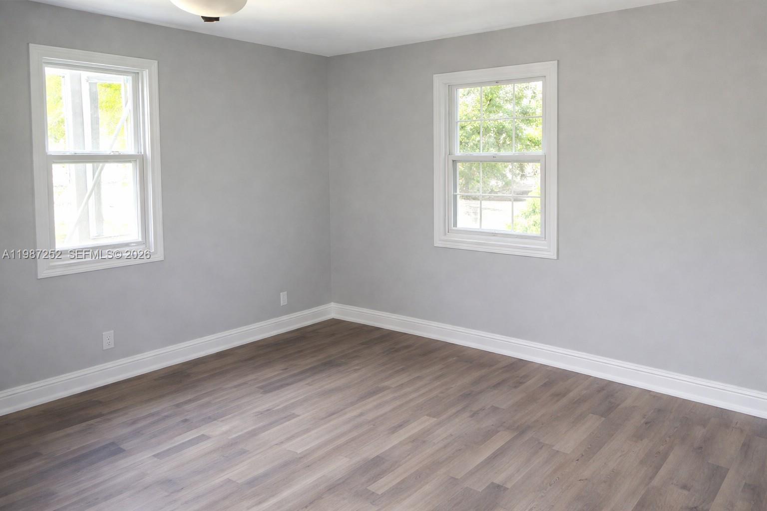 An empty room features gray walls, white trim, and wood-look flooring with two windows — 4541 SW 28th Ter, Dania Beach FL 33312, DANIA BEACH, FL