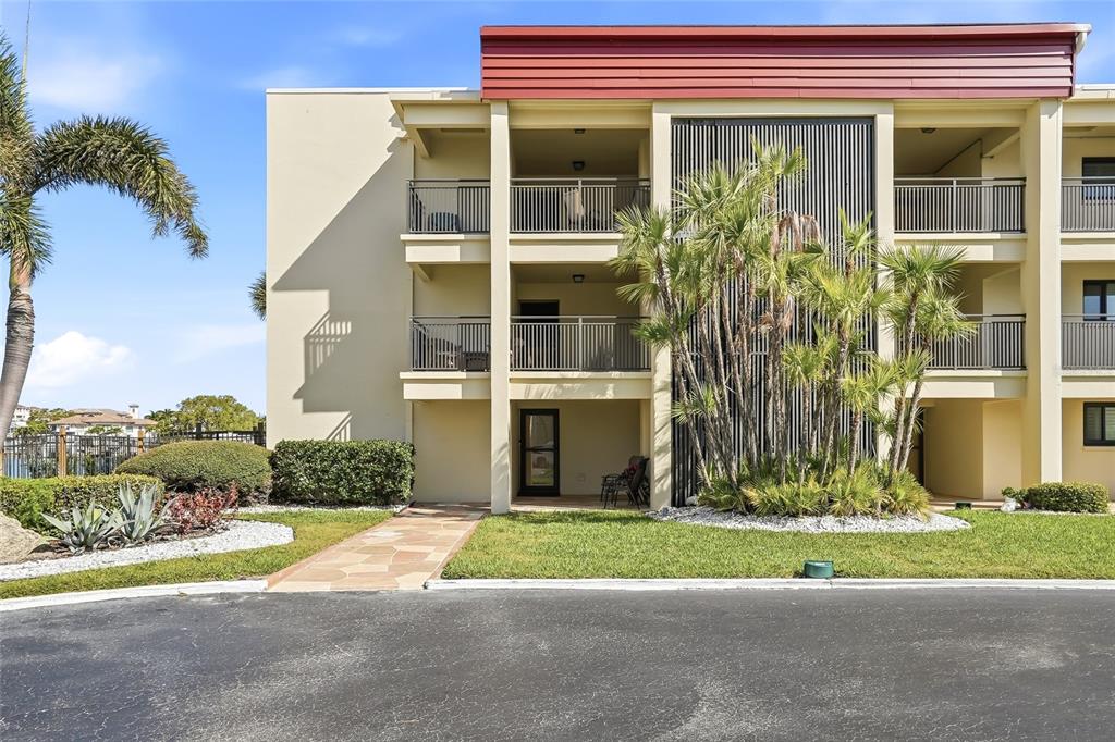 A three-story apartment building features balconies, a stone walkway, and palm trees in front — 868 BAYWAY BOULEVARD UNIT 101, CLEARWATER BEACH, FL