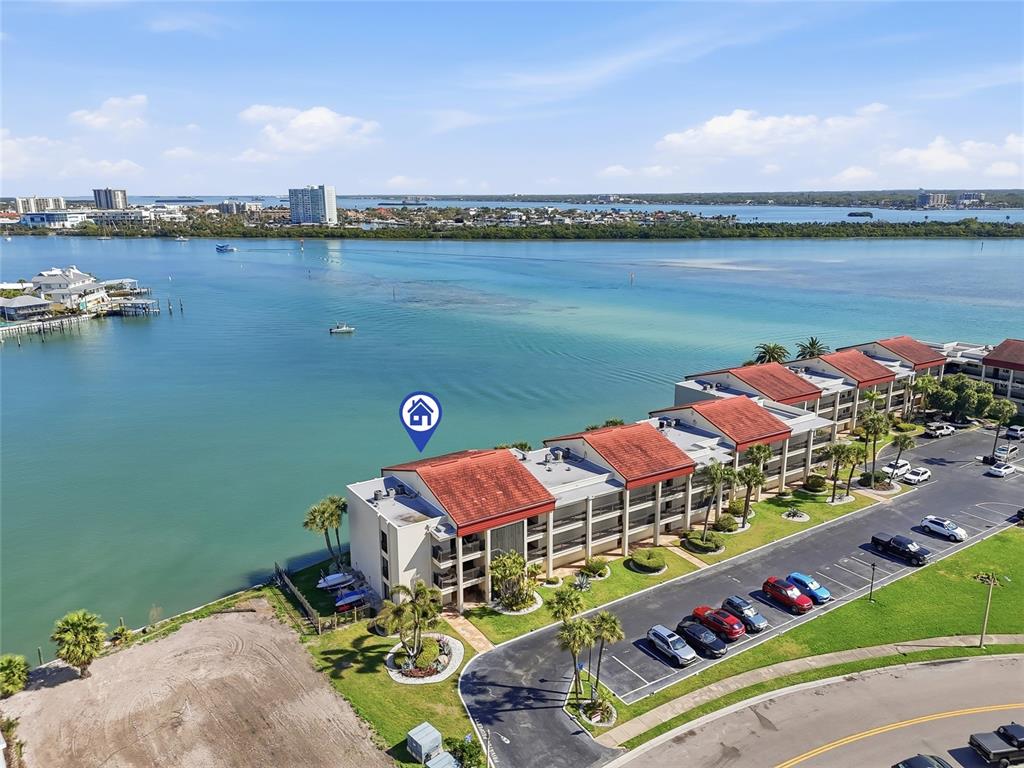 An aerial view shows a multi-story waterfront condominium building with red roofs and parking — 868 BAYWAY BOULEVARD UNIT 101, CLEARWATER BEACH, FL