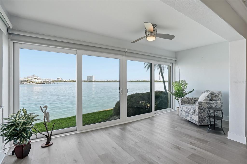 A sunroom with light wood-look flooring, a ceiling fan, and large sliding glass doors overlooking water — 868 BAYWAY BOULEVARD UNIT 101, CLEARWATER BEACH, FL