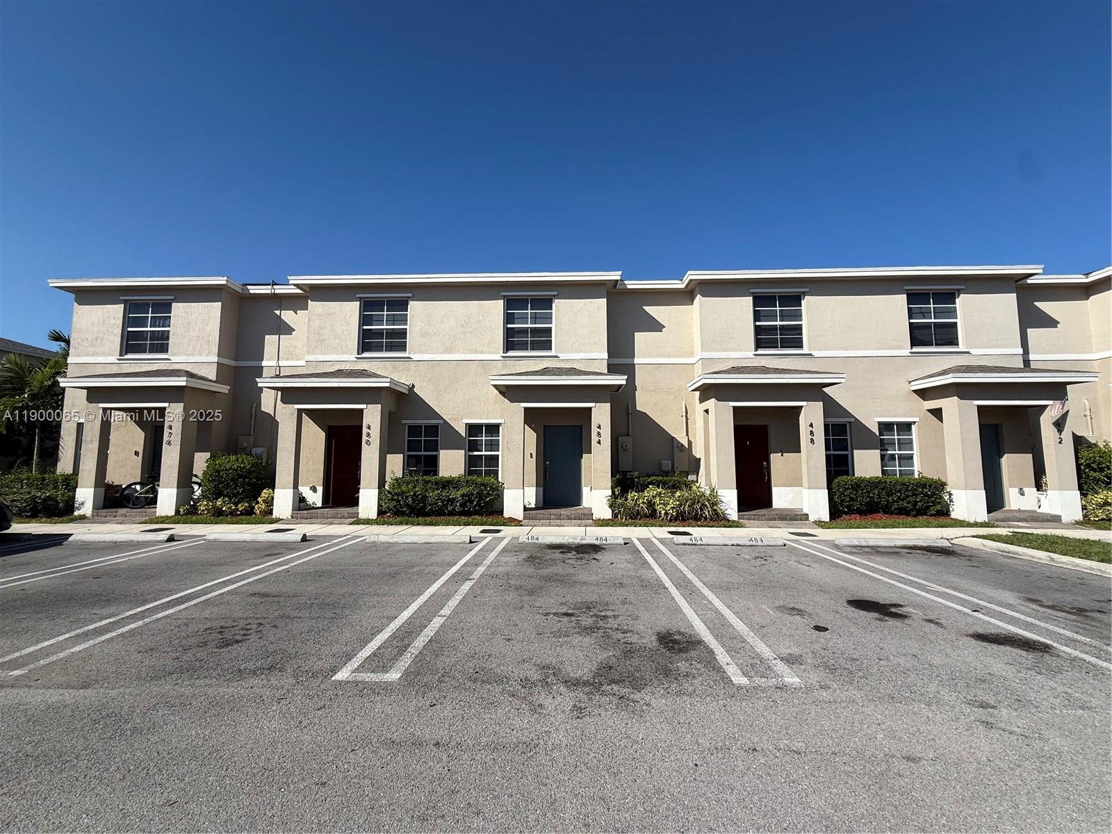 A row of two-story townhomes with beige stucco exteriors and assigned parking spaces in front — 484 NE 5th St, Florida City FL 33034, FLORIDA CITY, FL