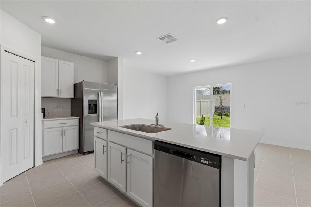 A modern kitchen features white cabinets, stainless steel appliances, a center island, and tile flooring — 7847 ABAGAIL DRIVE, LAKELAND, FL