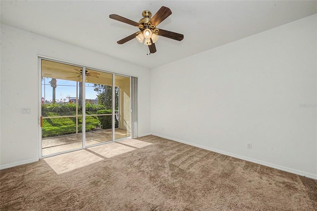 An empty bedroom with brown carpet, a ceiling fan, and sliding glass doors to a patio — 11443 52ND COURT E, PARRISH, FL