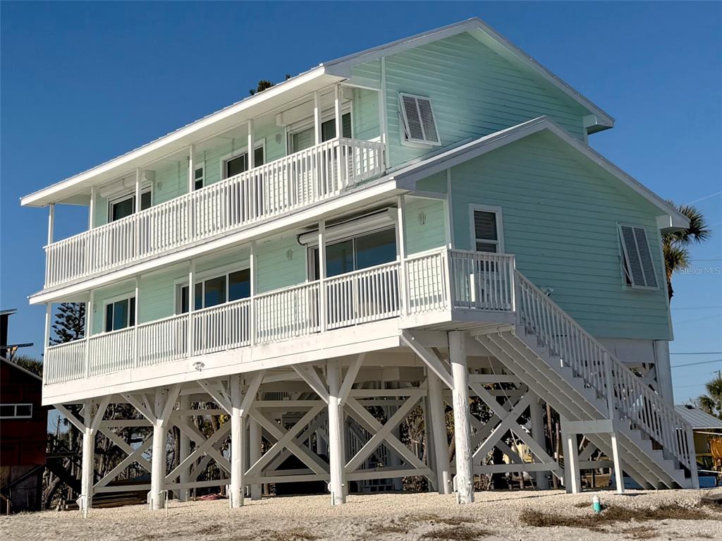 A light green, elevated beach house with white railings and an outdoor staircase — 6780 MANASOTA KEY ROAD, ENGLEWOOD, FL