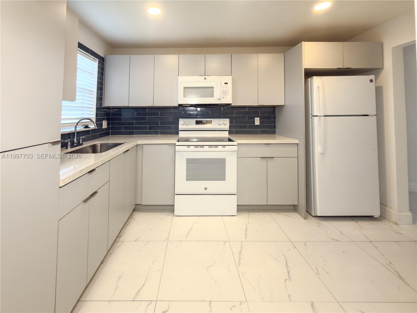 A view from a hallway looking into a kitchen with white cabinets and tile flooring — 605 S State Road 7 # 1D, Margate FL 33068, MARGATE, FL