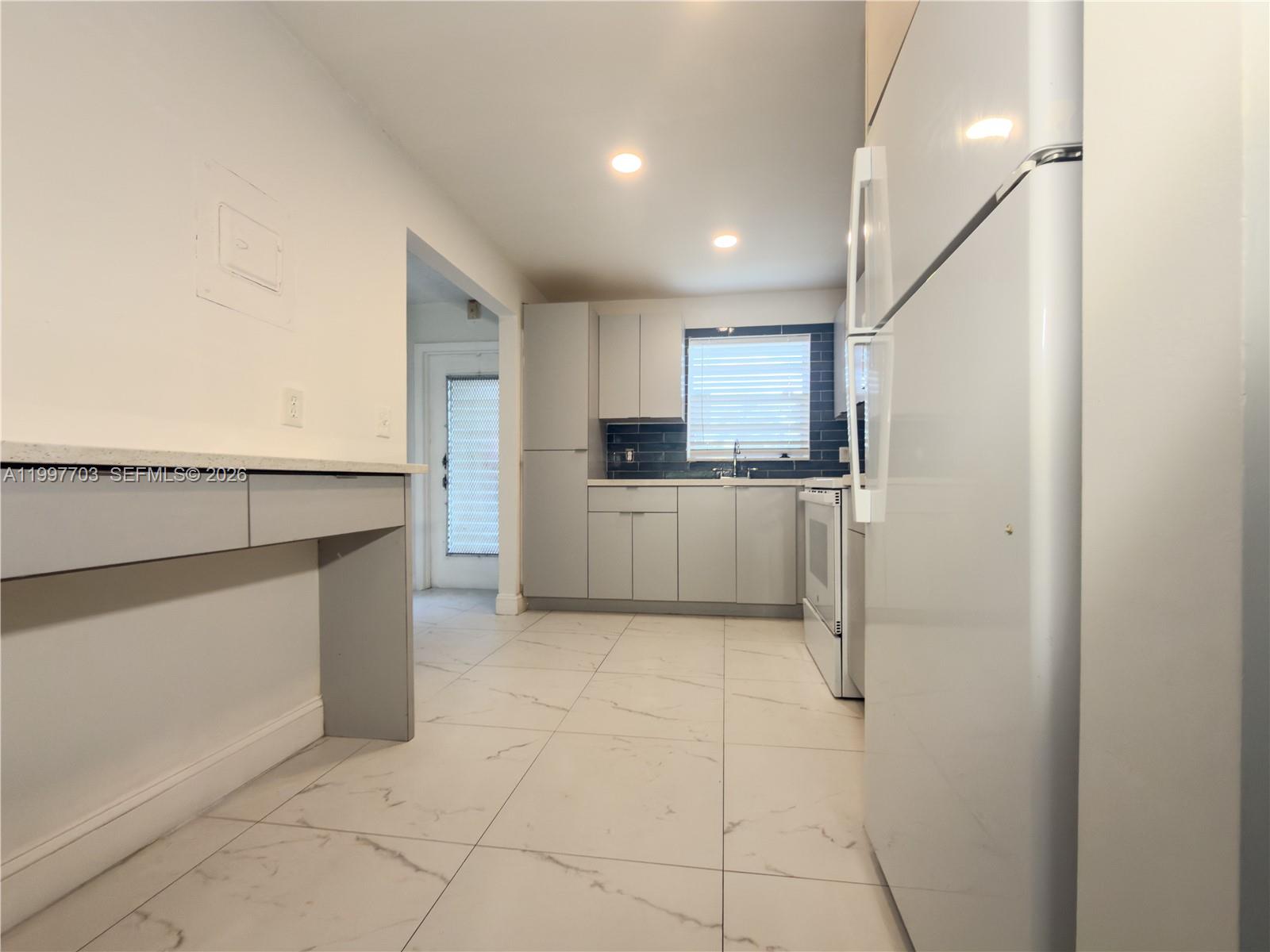 A kitchen features light gray cabinets, white appliances, dark blue tile backsplash, and marble-look flooring — 605 S State Road 7 # 1D, Margate FL 33068, MARGATE, FL