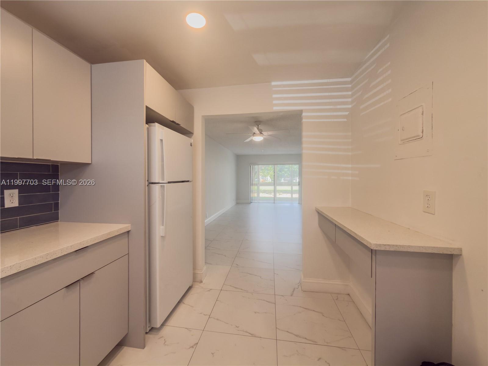A kitchen features light gray cabinets, white countertops, white appliances, and white marble-patterned tile flooring — 605 S State Road 7 # 1D, Margate FL 33068, MARGATE, FL