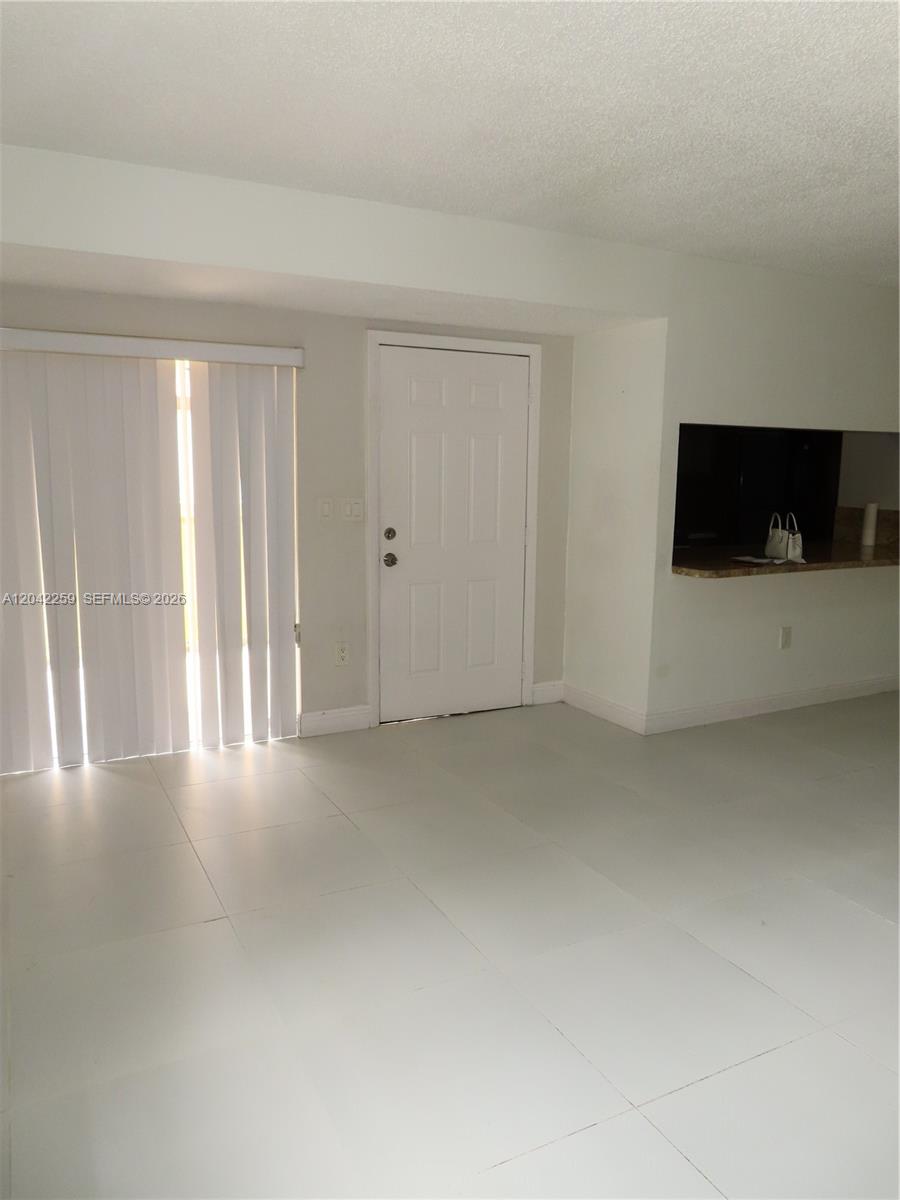 A room with white tile floors, a white door, vertical blinds, and a kitchen pass-through — 13894 SW 65th Ter # 12, Miami FL 33183, MIAMI, FL