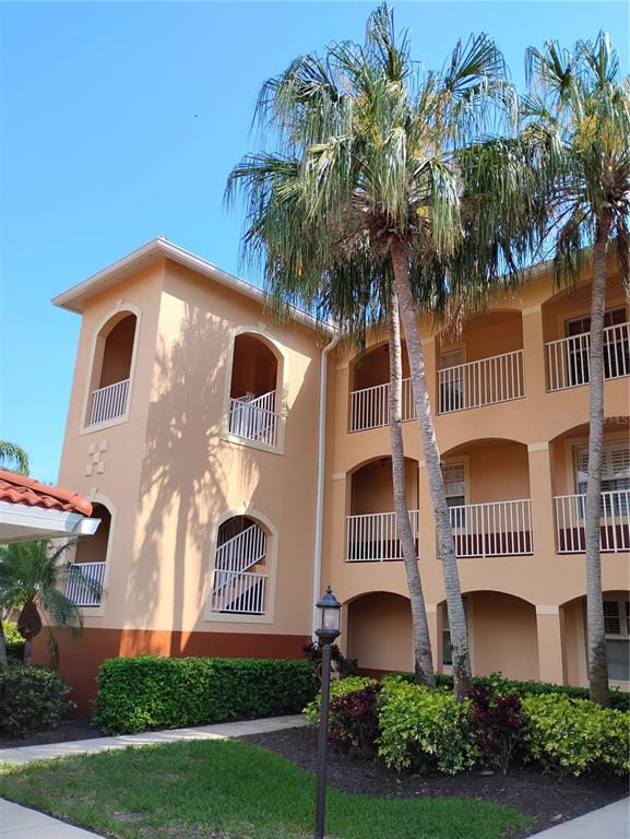 A three-story apartment building with peach-colored stucco walls, arched balconies, and tall palm trees — 1761 AUBURN LAKES DRIVE UNIT 11, VENICE, FL