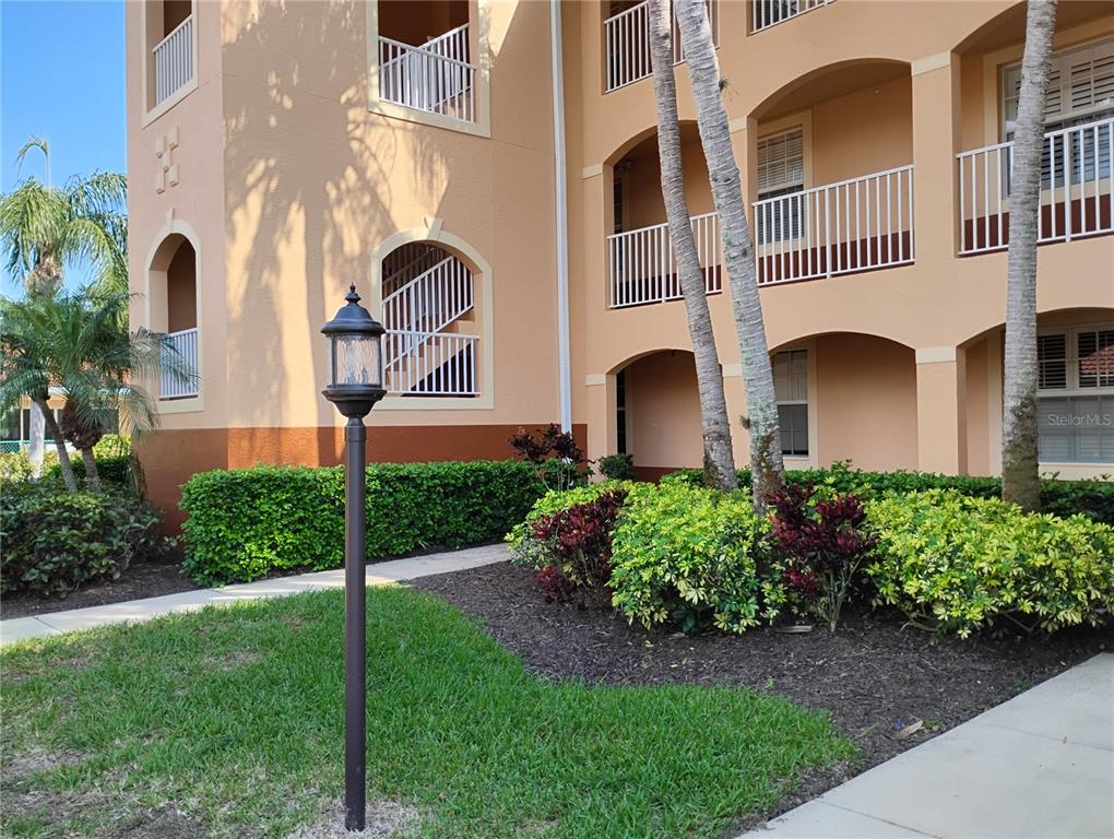 A multi-story tan apartment building features arched balconies, white railings, and landscaped bushes — 1761 AUBURN LAKES DRIVE UNIT 11, VENICE, FL