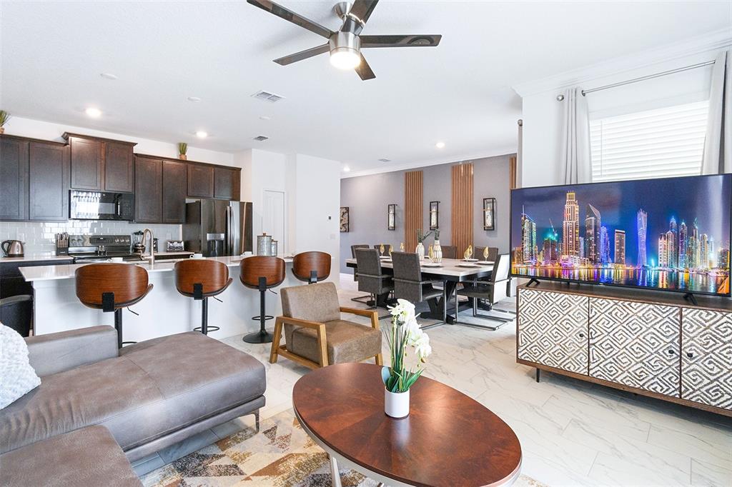 An open-concept living area features a kitchen with dark cabinets, a dining space, and television — 3011 PENELOPE LOOP, KISSIMMEE, FL