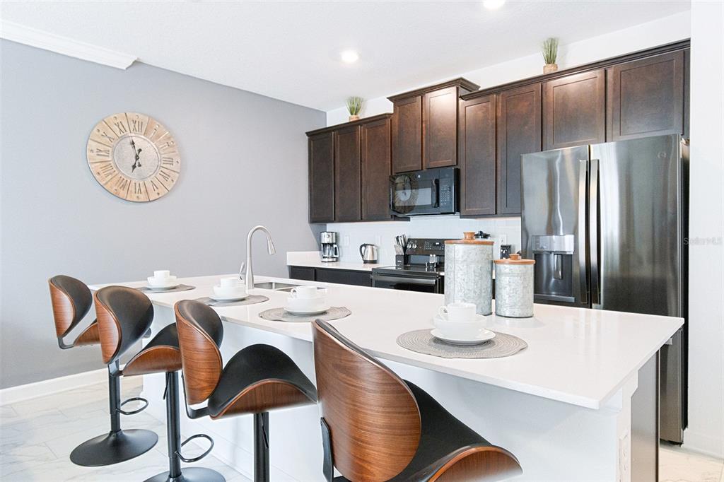 A kitchen features dark wood cabinets, stainless steel appliances, and a white quartz island — 3011 PENELOPE LOOP, KISSIMMEE, FL