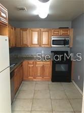 A kitchen features light wood cabinets, a black stove, a microwave, and tiled flooring — 3984 VERSAILLES DRIVE UNIT 3984C, ORLANDO, FL