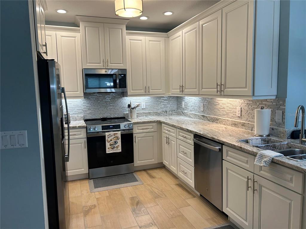 A kitchen features white cabinets, granite countertops, stainless steel appliances, and light wood-look flooring — 3426 79TH STREET CIRCLE W UNIT 203, BRADENTON, FL