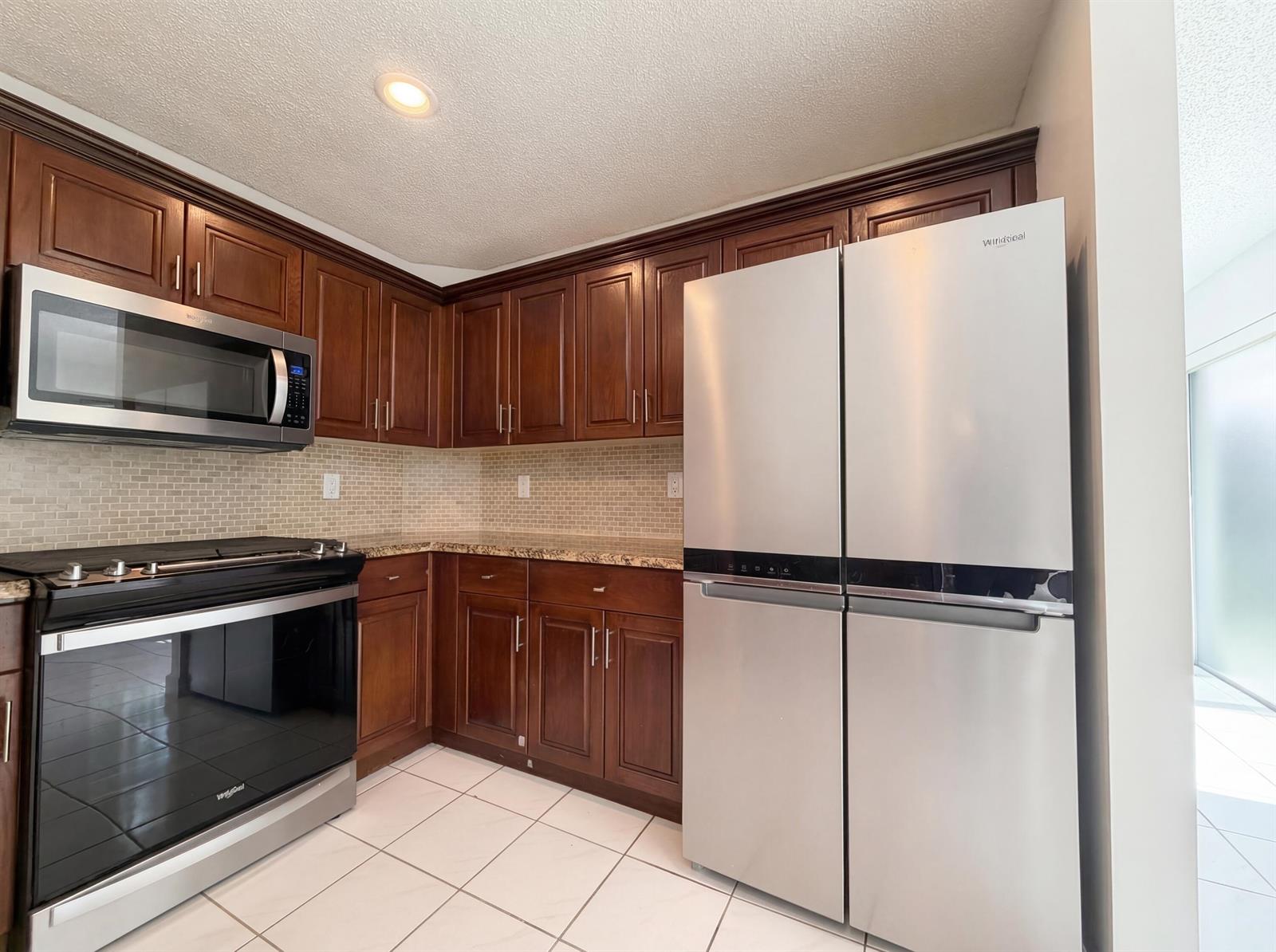 A kitchen features dark wood cabinets, stainless steel appliances, granite countertops, and tiled flooring — 73 Gables Boulevard, Weston FL 33326, WESTON, FL