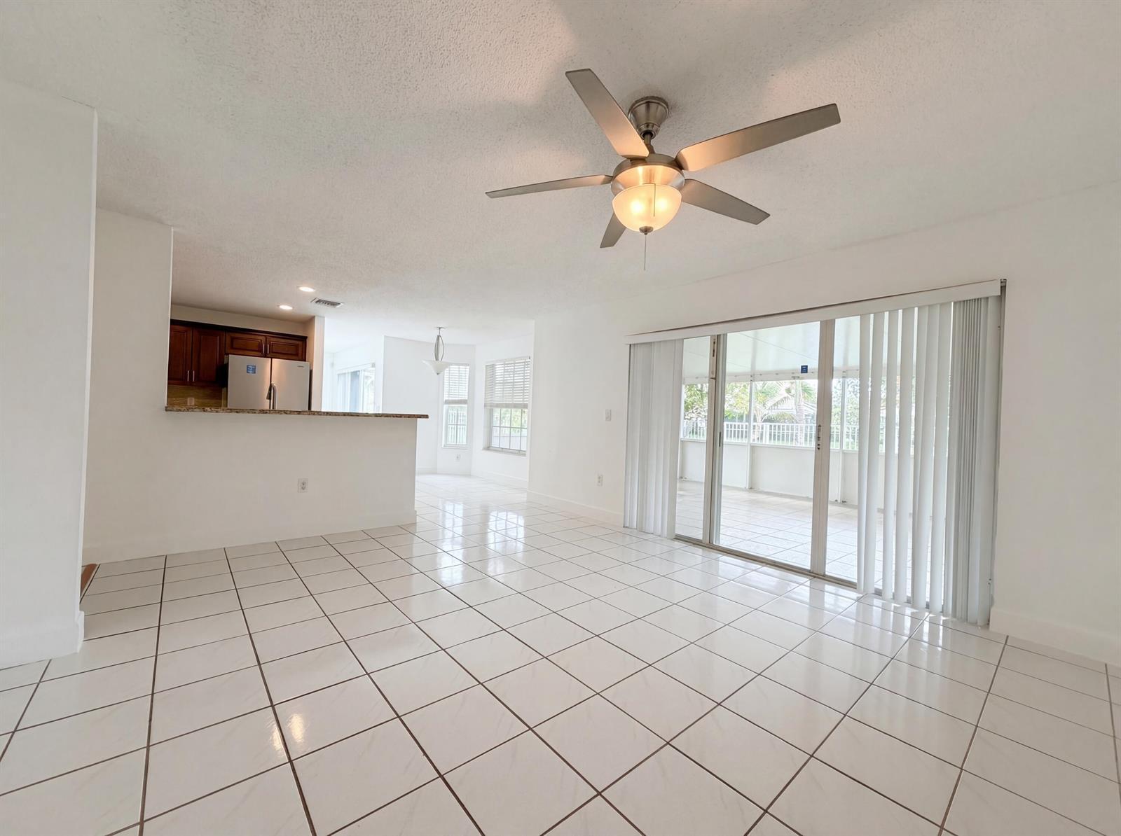An open-concept living area features white tile flooring, a ceiling fan, and sliding glass doors — 73 Gables Boulevard, Weston FL 33326, WESTON, FL