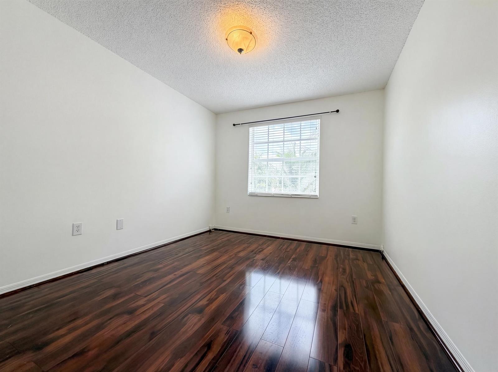 An empty bedroom features white walls, dark wood-look flooring, and a single window — 73 Gables Boulevard, Weston FL 33326, WESTON, FL