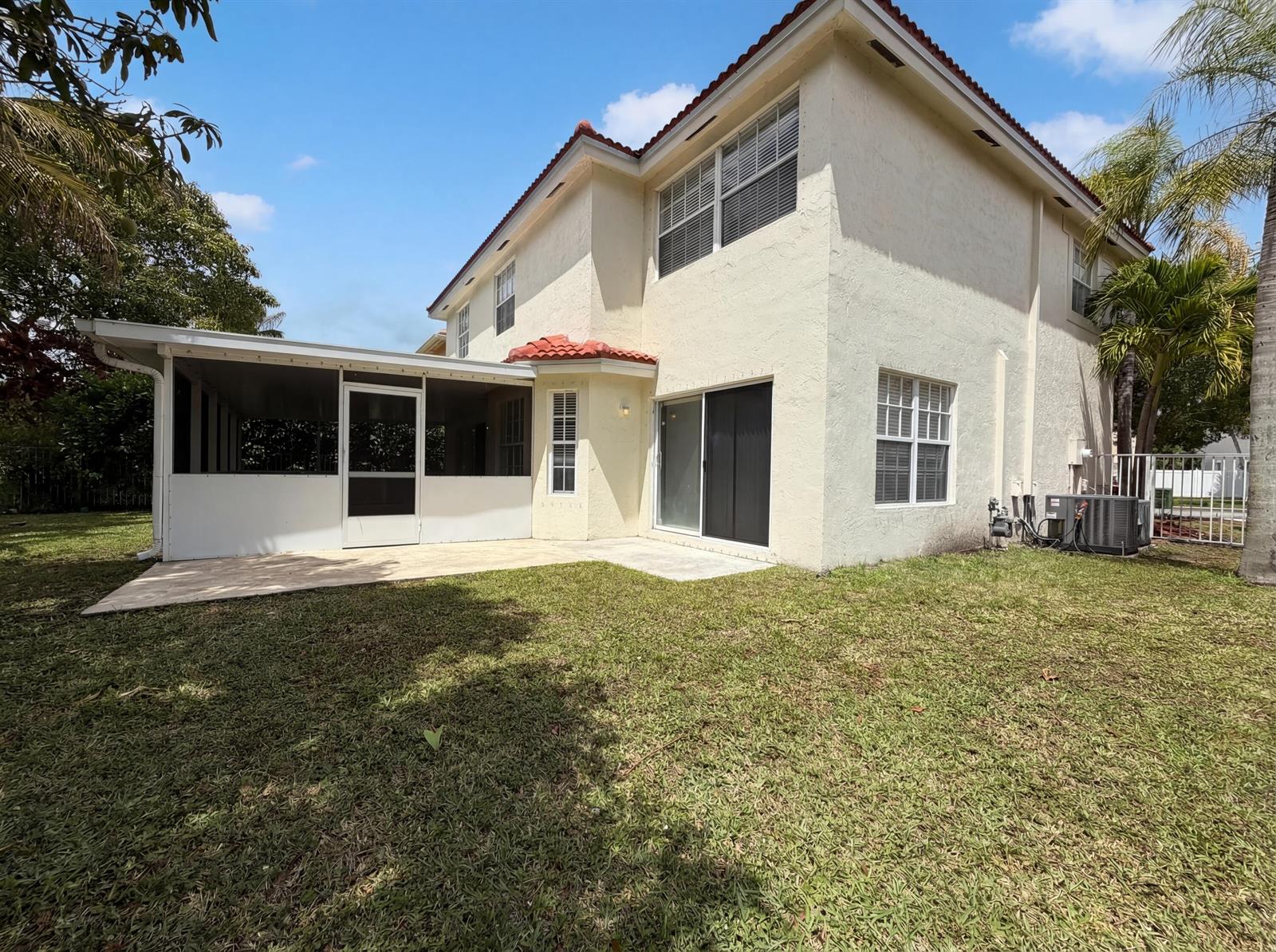 The exterior of a two-story stucco house features a screened-in patio and a grassy backyard — 73 Gables Boulevard, Weston FL 33326, WESTON, FL