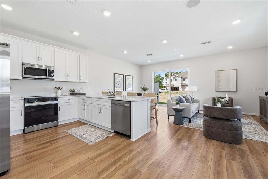 A modern open-concept kitchen and living area with white cabinetry, stainless appliances, and wood flooring — 11363 BRILEY MAY WAY, RIVERVIEW, FL